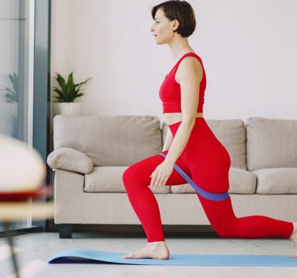 Side view of fit female in sportswear with short hair doing exercise with elastic band on blue mat near sofa in living room